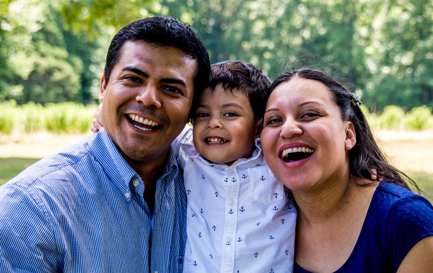 Latino family of three, parents holding young son, all with big smiles